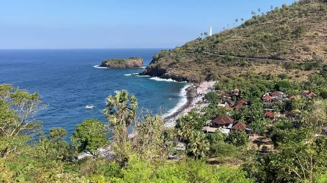 Scenic view of Amed coastal village and bay with white lighthouse on the green hill in East Bali, Indonesia