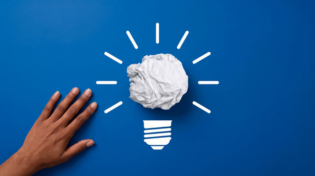 Creative business idea concept with a crumpled paper lightbulb and a human hand on a solid blue background