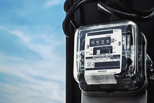 Analog electricity watt hour meter installed on a utility pole against a clear blue sky. Concept of household power consumption and energy costs.