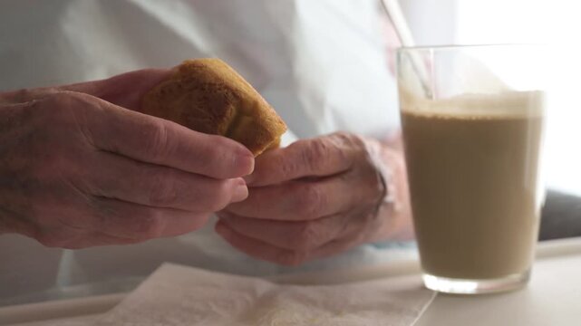 Close up of elderly woman hands holding and breaking soft cake next to coffee