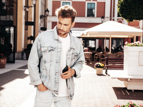 Portrait of handsome confident stylish hipster lambersexual model. Sexy man dressed in jeans jacket. Fashion male posing in the street in sunglasses in Europe city. Outdoors at sunset