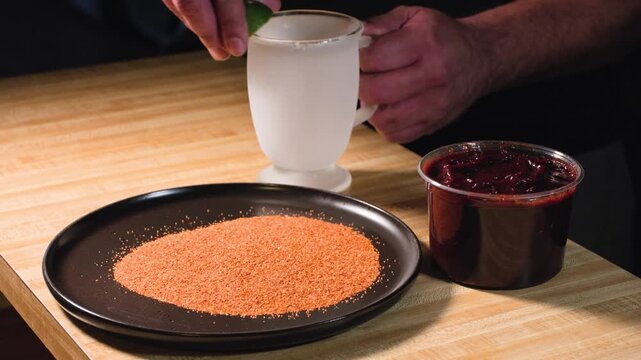 Close up cooking footage showing man rimming a frosted cup with lime, chamoy and tajin during a homemade chamoy sauce recipe prepared from scratch