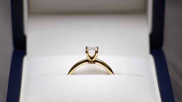 Wedding ring in a box being opened up. Engagement ring revealed, marriage proposal. Emerald cut diamond yellow gold knife edge