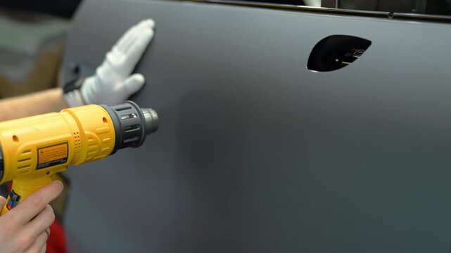 Close up footage of process of installed vinyl film on a car body in a workshop. detailing process with film installation, smooth matte finish and precision work