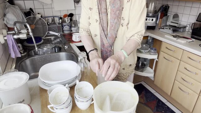 Woman transfers dishes, glasses and kitchen utensils from the sink to the countertop while organizing them before washing. Static Medium Shot