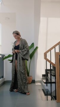 Elegant woman wearing luxury kimono robe over  swimsuit in modern tropical villa.