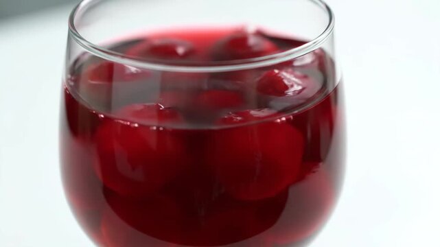 Close-up Macro Shot of Vibrant Red Cherries Soaked in Sweet Syrup or Juice Inside a Glass, Ideal for Cocktail Garnish or Dessert Toppings on a Bright Background