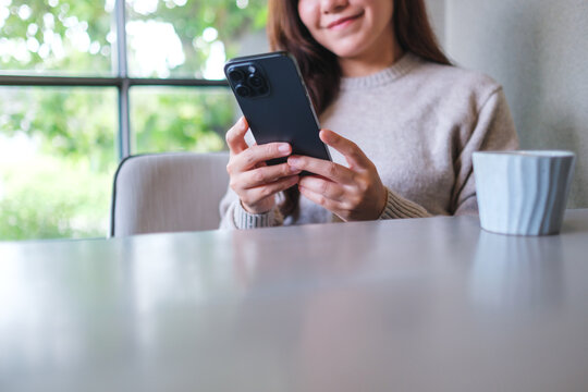 Closeup image of a woman holding and using mobile phone in cafe