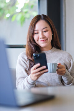 Vertical portrait image of a businesswoman drinking coffee while using mobile phone and laptop computer