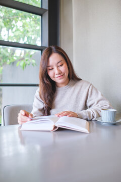 Vertical portrait image of a woman reading a book with coffee cup on the table