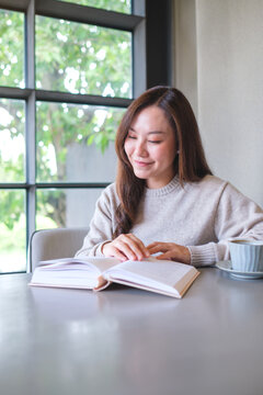 Vertical portrait image of a woman reading a book with coffee cup on the table