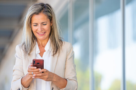 middle-aged businesswoman walking down the street looking at a mobile phone or smartphone