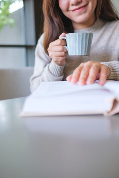 Vertical closeup image of a woman reading a book and drinking coffee