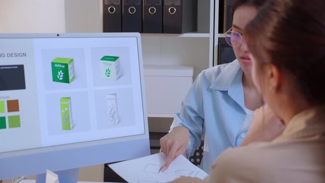 Two asian businesswoman working packaging design with ai computer, team business woman meeting of paper sketch drawing mockup holding prototype product box, creative packaging design project.
