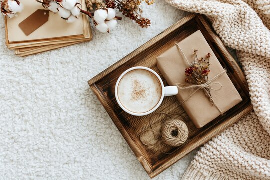 Cozy morning with a coffee cup and gift on a rustic tray with a knitted blanket