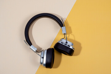Naklejka premium Computer peripherals—keyboard, mouse, wireless headphones—are placed on a yellow and cream-colored background.