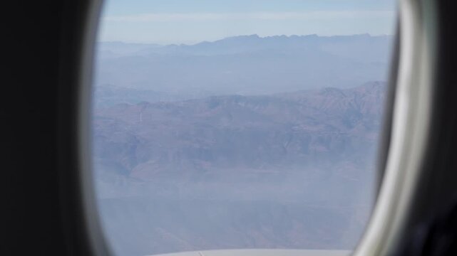 view through airplane window while flying over mountain range over Kunming area in China over cloud and mountain submit in daytime,high plains of china near Tibet area from airplane