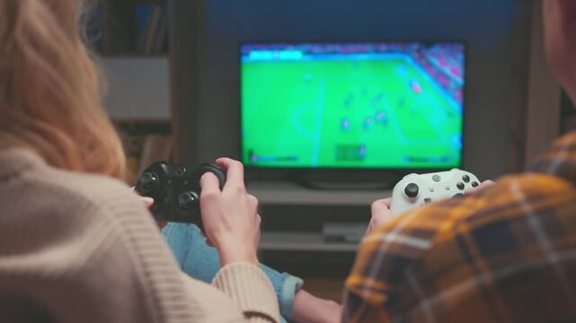 Television Screen Showing Soccer Match with Gamers Holding Controllers. Unrecognizable Couple Plays Virtual Football Game on Console at Night. Cyber Sport Entertainment Technology 4k