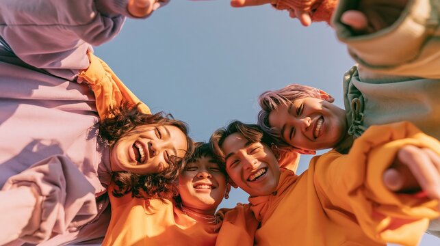 Diverse group of young friends in colorful hoodies embracing happily in a circle with sky background