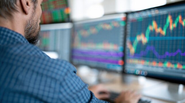 Trader monitoring financial market charts and stock exchange data on multiple computer screens