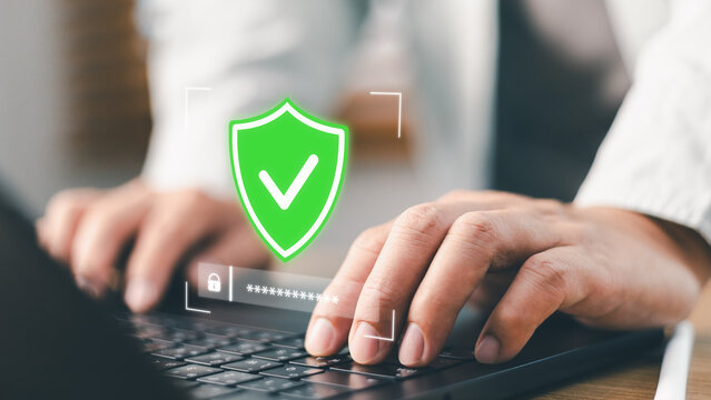 Businessman typing password on laptop with green shield check mark icon. Concept of cyber security, data protection, network safety, firewall encryption, and secure internet access