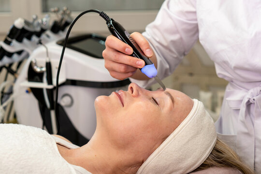 Ultrasonic skin scrubber used on forehead during professional facial skin care procedure.