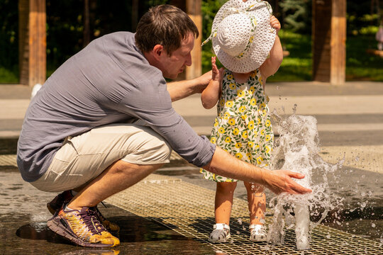 Father Helping Toddler Daughter Play in Splash Fountain