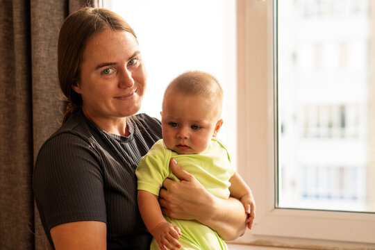 Mother Holds Thoughtful Baby Son Beside Bright Window