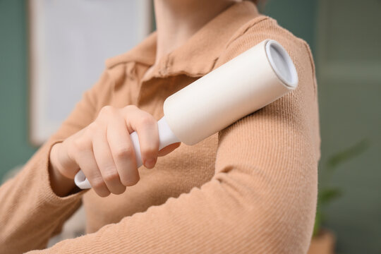 Person using a white lint roller to clean a beige ribbed sweater, removing dust and pet hair from clothing, this household chore maintains clothing freshness and appearance