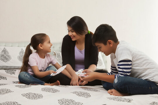 Mother playing card game with children in bed and having fun together