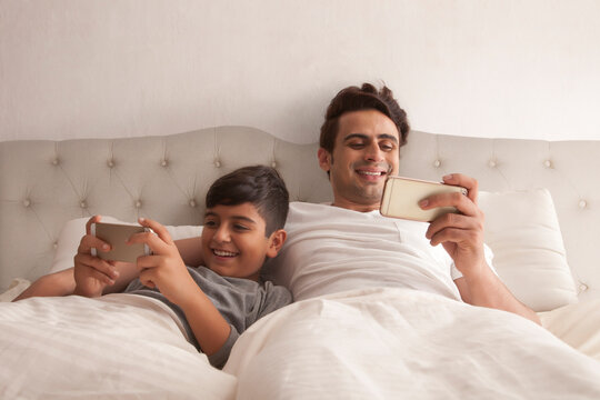Smiling father and son using mobile phone on bed in bedroom