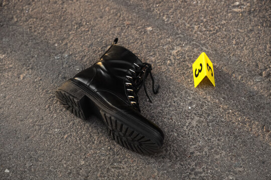 Black combat boot and yellow evidence marker number three on asphalt, crime scene investigation
