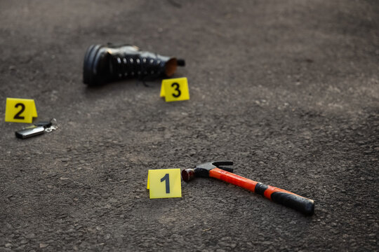 Crime scene evidence markers with hammer, boot, and car keys on asphalt, forensic investigation