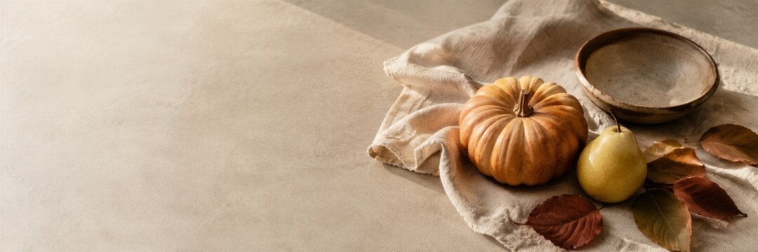 Small pumpkin with fresh pear and empty ceramic bowl on linen cloth. Autumn harvest still life with dry leaves on stone table.