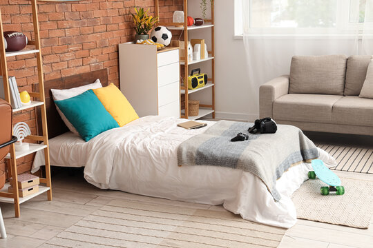 Teenage boys bedroom with a single bed, brick wall, and modern decor, gaming accessories and sports equipment