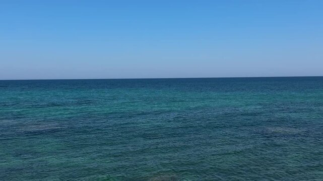 Peaceful view of a sailing yacht on the turquoise Adriatic Sea near the rocky shoreline of Monopoli, Apulia, Italy under a clear blue summer sky. Coastal landscape, travel destination, vacation, copy 