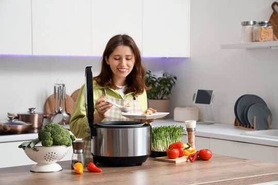 Smiling young woman serving food from a modern multi cooker in a bright kitchen with Fresh vegetables