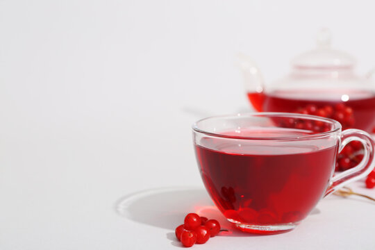 Glass cup of hot viburnum tea and berries on grey background