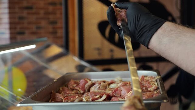 A detailed view of a chef in gloves, preparing shish kebab in a restaurant or kebab shop. The act of preparing shish kebab.