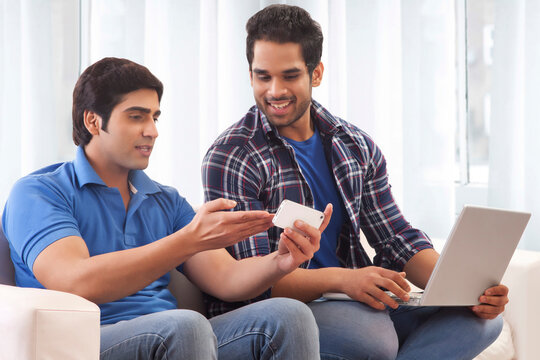 Two friends looking at mobile phone while using laptop
