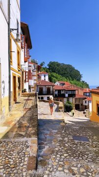 woman tourist wearing hat walking down cobbled street in lastres coastal village in Lastres spain