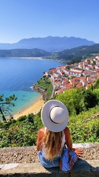 woman tourist wearing hat looking at lastres coastal village beach and ocean view in asturias spain