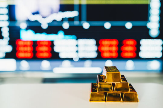 Stack of shiny gold bars on table with blurred stock market chart background. Ideal for financial investment, wealth management, commodity trading, and economy commercial concepts.