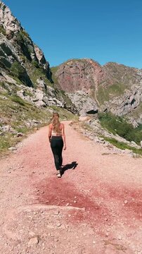 female hiker walking along red dirt mountain trail under clear blue sky, vertical video