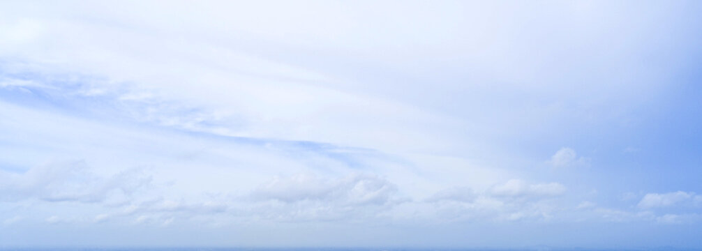 Wide panoramic view of bright light blue sky with soft white wispy clouds, natural clear daytime atmosphere texture backdrop for website header banner and background.