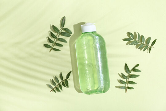 Bottle of micellar water and leaves on green background