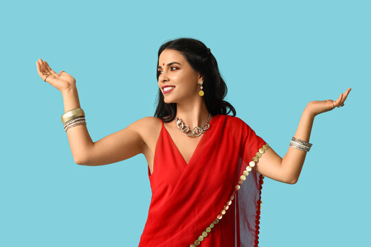 Beautiful young happy Indian woman in traditional sari dancing on blue background. Divaly celebration