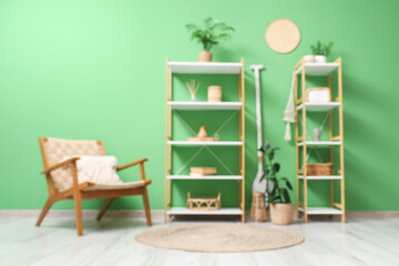 Fototapeta premium Blurred view of living room with shelving units and wooden armchair near green wall