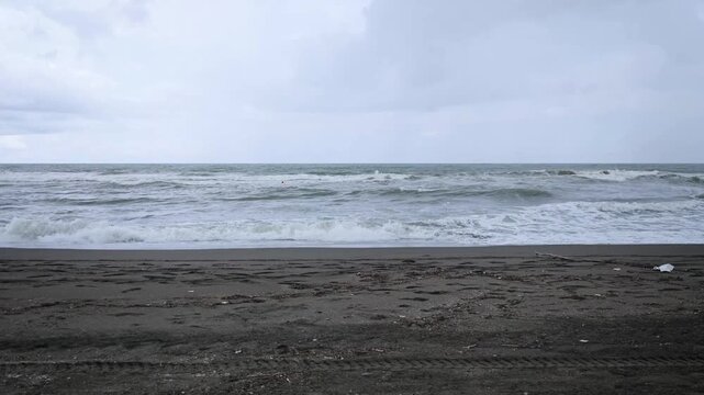 Rough Sea Waves Rolling onto Empty Dark Sand Shoreline on Cloudy Day