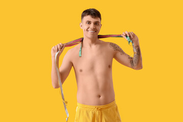 Fototapeta premium Young man with measuring tapes on yellow background. Weight loss concept